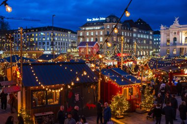 3-12-2024 Zürih, İsviçre. Sechselautenplatz Noel pazarındaki dükkanları ziyaret eden insanlar. Mavi saat geç akşam, Noel ışıkları.