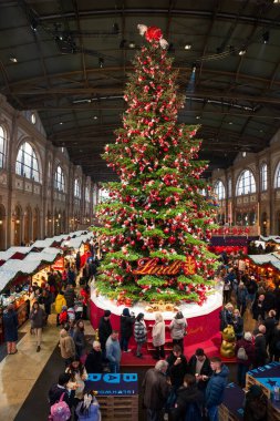 17-12-2024 Zurich, Switzerland. Large Christmas tree inside Zurich main station decorated with red Lindt chocolate balls. Wide-angle view, people in the background clipart