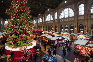 17-12-2024 Zurich, Switzerland. Large Christmas tree inside Zurich main station decorated with red Lindt chocolate balls. Wide-angle view, people in the background clipart