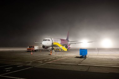 27-12-2024 Timisoara Traian Vuia International Airport, Romania. Lufthansa City commercial airplane on the runway waiting to be serviced on a foggy winter night. People deboarding in the background. clipart