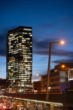 24-01-2025 Zurich, Switzerland. Prime Tower glass skyscraper office building at blue hour. Illuminated offices, city traffic and overpass at the bottom. clipart