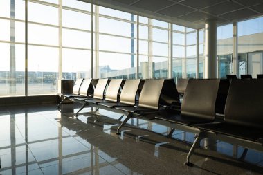 Uluslararası havaalanı terminalinde boş koltuk ve banklar. Kalkış bekleme odası kapının yanında. Büyük pencereler, doğal ışık, insan yok..