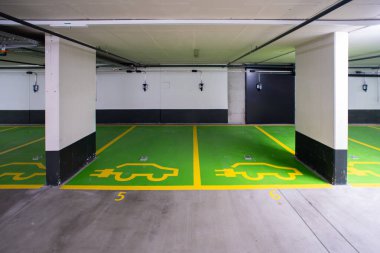 Elektrikli arabalar için ayrılmış park yerleri olan boş bir yeraltı otoparkı. Yeşil boya, arka planda şarj aletleri, insan yok..