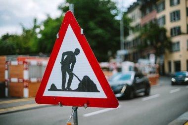 Yol üçgen yol işareti ile çalışıyor. Yakın çekim, sığ alan derinliği, gündüz, arka planda bulanık şehir manzarası, yanından geçen bulanık araba.