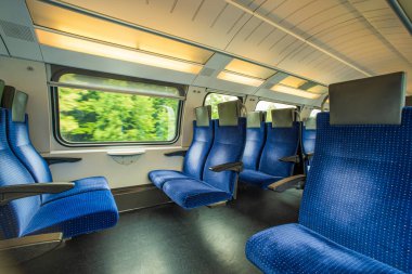 Avrupa 'daki yolcu treninin içinde boş mavi kumaş koltuklar. Geniş pencere kenarı koltukları, hareket eden tren, bulanık kırsal arka plan, insan yok..