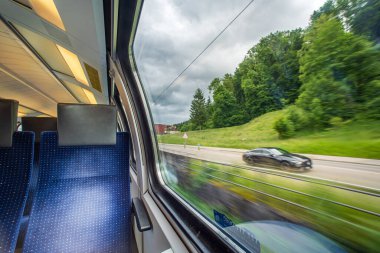 Avrupa 'daki yolcu treninin içinde boş mavi kumaş koltuklar. Geniş pencere kenarı koltukları, hareket eden tren, bulanık kırsal arka plan, insan yok..
