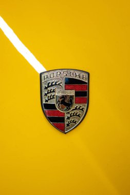 Porsche kaput ya da kaput amblemi ya da rozet. Üstten aşağı, yakın görüş, sarı araba, insan yok.