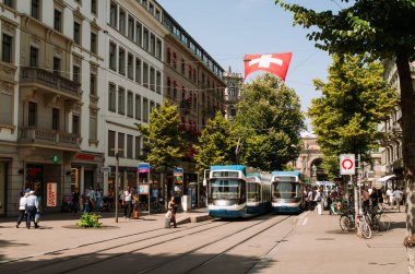 16-06-2025 Zürih, İsviçre. 6 ve 7 numaralı tramvay ana istasyon yakınlarındaki Bahnhofstrasse istasyonundan yolcu alıyor. Güneşli bir yaz günü, yayalar