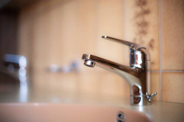 Daire banyosunun içinde parlak, krom su musluğu. Yakın çekim, sığ alan derinliği, insan yok.