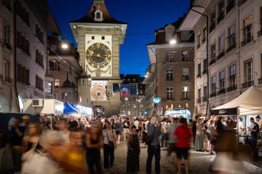 07-08-2025 Bern, İsviçre. Kalabalık sokak yemeklerinin ve Buskers sokak müzik festivalinin tadını çıkarıyor. Mavi saat ışığı, uzun pozlama, bulanık insanlar, geniş açı.