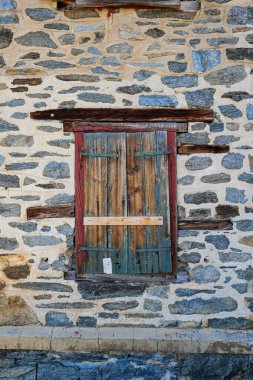 Kapalı ahşap pencere perdeleri ya da kepenkleri olan çok eski taş bir bina.