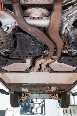 Egzoz sistemi, tekerlekleri ve dingil parçaları olan bir araba şasisi. Geniş açı, manzaralı, asansörlü araç, tamirhanenin içinde insan yok.