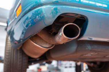 Tek egzozlu egzoz borusu ve tamirhanedeki kaldırılmış araba için bahşiş. Yaklaş, geniş açı, manzaraya bak, insan yok.