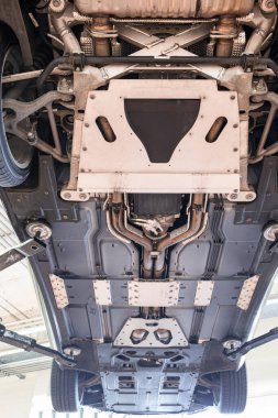 Egzoz sistemi, tekerlekleri ve dingil parçaları olan bir araba şasisi. Geniş açı, manzaralı, asansörlü araç, tamirhanenin içinde insan yok.