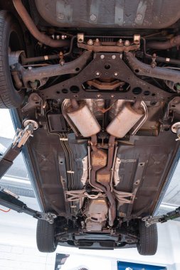Egzoz sistemi, tekerlekleri ve dingil parçaları olan bir araba şasisi. Geniş açı, manzaralı, asansörlü araç, tamirhanenin içinde insan yok.