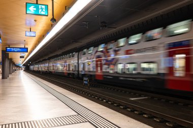 Zürih, İsviçre, 19 Ağustos 2025. Bulanık, hareket eden yolcu treni ve yeraltı ana istasyon platformunda bekleyen insanlar.