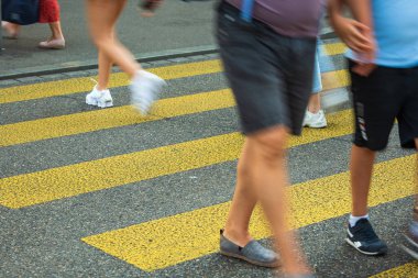 Sarı zebra ya da yaya geçidinden geçen insanların bulanık, tanınamaz bacakları. İnsanların belden aşağı görüntüsü, asfalt üzerinde ayaklar ve bacaklar, güneşli yaz günü, hareket bulanıklığı