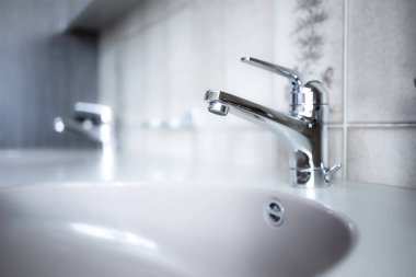 Daire banyosunun içinde parlak, krom su musluğu. Yakın çekim, sığ alan derinliği, insan yok.