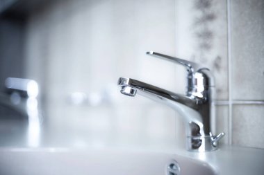 Daire banyosunun içinde parlak, krom su musluğu. Yakın çekim, sığ alan derinliği, insan yok.