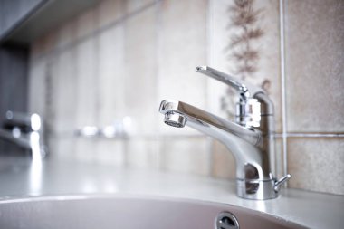 Daire banyosunun içinde parlak, krom su musluğu. Yakın çekim, sığ alan derinliği, insan yok.