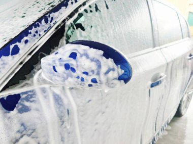 Oto yıkamada köpükle kaplanmış mavi araba, detaylı çekim, geniş açı, insan yok.