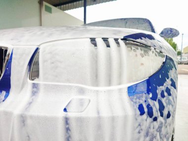 Oto yıkamada köpükle kaplanmış mavi araba, detaylı çekim, geniş açı, insan yok.