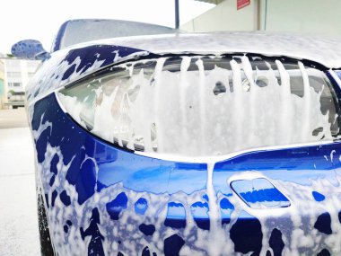 Oto yıkamada köpükle kaplanmış mavi araba, detaylı çekim, geniş açı, insan yok.