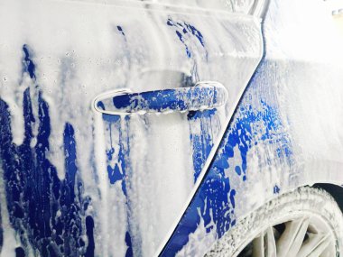 Oto yıkamada köpükle kaplanmış mavi araba, detaylı çekim, geniş açı, insan yok.