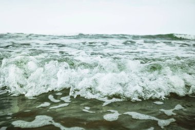 Kıyıya ulaşan küçük, köpüklü gelgit dalgaları, alçak açı, su seviyesi, bulutlu yaz günü, insan yok.