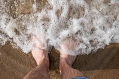 Beyaz erkek çıplak ayakla kotları kaldırdı ve kumlu bir sahilde sığ gel-git dalgaları ile kıyıya ulaşan deniz suyu üzerinde duruyordu. Üstten aşağı, görünümü kapat