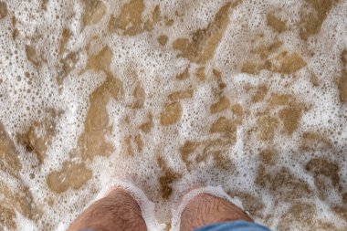 Beyaz erkek çıplak ayakla kotları kaldırdı ve kumlu bir sahilde sığ gel-git dalgaları ile kıyıya ulaşan deniz suyu üzerinde duruyordu. Üstten aşağı, görünümü kapat