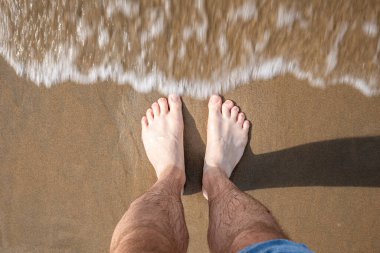 Beyaz erkek çıplak ayakla kotları kaldırdı ve kumlu bir sahilde sığ gel-git dalgaları ile kıyıya ulaşan deniz suyu üzerinde duruyordu. Üstten aşağı, görünümü kapat