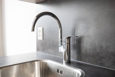 Closed, new, stainless water tap faucet and sink in apartment kitchen. Bright, natural window light, selective focus, top down view, no people