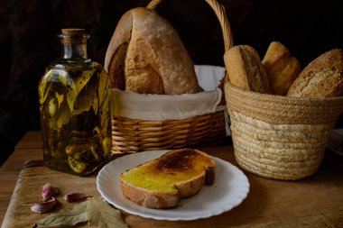 Classic still life with extra virgin olive oil, garlic, bread in a basket and a plate with a slice of toasted bread with olive oil. Ingredients of a typical breakfast of the Mediterranean diet.