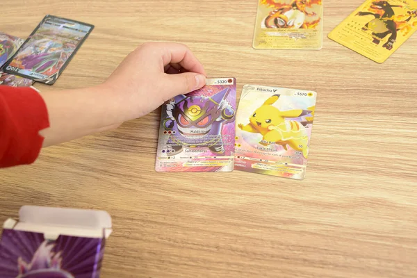 Arahal. Sevilla. İspanya. 1 Mart 2023. Nadir bulunan Pokemon kartlarını ahşap bir masanın üzerine koyan bir çocuğun ellerinin ayrıntıları. Pokemon anime serisine dayanan koleksiyon kartları.