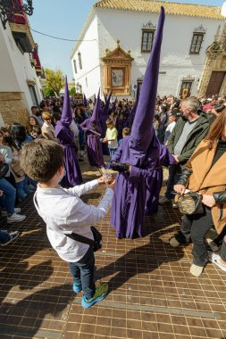 Arahal. Sevilla. İspanya. 15 Nisan 2022. Çocuk bir balmumu topu yapmak için tövbe edenden balmumu ister. Kutsal Cuma günü Nasıralı İsa Kardeşliği 'nin tövbekar alayı..