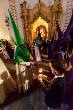Arahal. Sevilla. İspanya. 15 Nisan 2022. Çocuk bir balmumu topu yapmak için tövbe edenden balmumu ister. Arahal 'den (Sevilla) La Esperanza Kardeşliği' nin Tövbe Töreni, Kutsal Cuma günü.