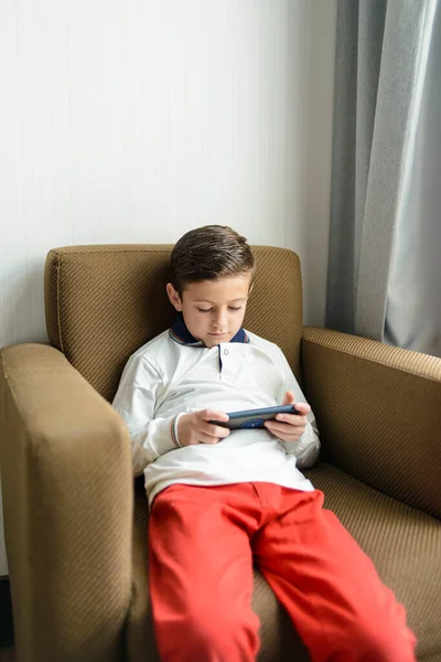 stock image Child using smartphone while sitting on a chair. Technology use by children and its consequences, including poor posture.