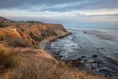 Güneş, Golden Cove 'un üzerinde batarken sakin suları, gökyüzünün ılık renklerini yansıtıyor. Rancho Palos Verdes, Kaliforniya' nın engebeli uçurumlarının arasında huzurlu bir kaçış sunuyor..