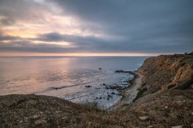 Güneş, Golden Cove 'un üzerinde batarken sakin suları, gökyüzünün ılık renklerini yansıtıyor. Rancho Palos Verdes, Kaliforniya' nın engebeli uçurumlarının arasında huzurlu bir kaçış sunuyor..