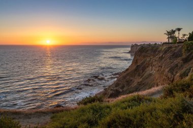 Güneş, Golden Cove 'un üzerinde batarken sakin suları, gökyüzünün ılık renklerini yansıtıyor. Rancho Palos Verdes, Kaliforniya' nın engebeli uçurumlarının arasında huzurlu bir kaçış sunuyor..