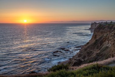 Güneş, Golden Cove 'un üzerinde batarken sakin suları, gökyüzünün ılık renklerini yansıtıyor. Rancho Palos Verdes, Kaliforniya' nın engebeli uçurumlarının arasında huzurlu bir kaçış sunuyor..