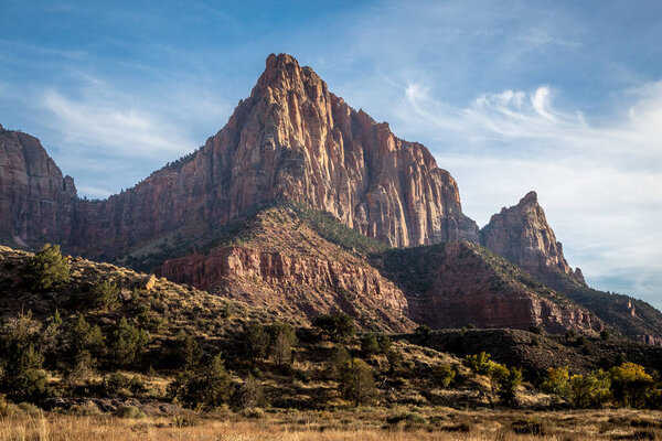 Watchman Mountain rises dramatically in the background, showcasing vibrant red sandstone cliffs against a clear blue sky.