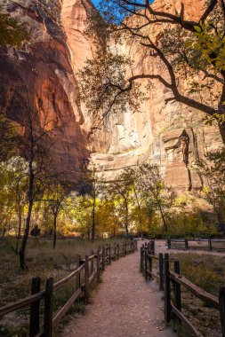 A peaceful path through Zion National Park, showcasing majestic sandstone cliffs and vibrant autumn foliage, inviting visitors to explore nature. clipart