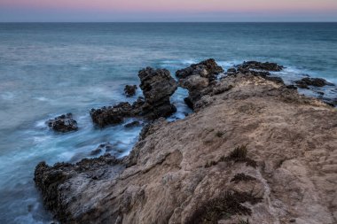 Rugged rock formations rise from the ocean at Leo Carrillo State Beach, as waves gently crash against the shore during twilight. clipart