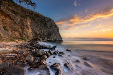 Gün batımında Crystal Cove 'daki kayalık sahilde dalgalar yavaşça süzülür, gökyüzü ve su boyunca ılık renkler bırakır..
