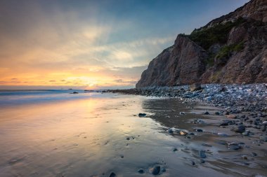 Güneş Dana Cove 'daki kayalıkların ardından batarken dalgalar yavaşça kıyıya vurur. Huzurlu atmosfer Kaliforniya kıyılarının güzelliğini yansıtıyor..