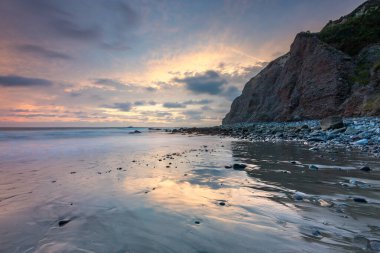 Vibrant sunset colors reflect on the calm waters of Dana Cove as waves gently lap against the shoreline of Dana Point, California. clipart