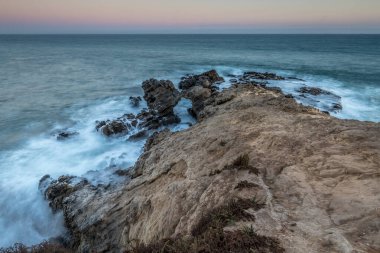Dalgalar, güneş ufukta batarken Malibu, Kaliforniya 'daki Leo Carrillo Eyalet Sahili' nin engebeli kayalarına çarpar..