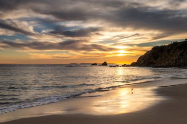 Güneş batarken dalgalar yavaşça kıyıya vurur, Laguna Beach, Orange County 'deki Crescent Bay Sahili' ne sıcak renkler bırakır..